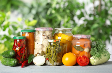 Fresh vegetables and jars of pickled products on wooden table