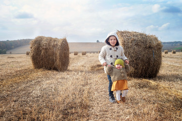 Naklejka na ściany i meble a boy and a girl near a haystack in a field at sun day on autumn next to a tractor cleans field