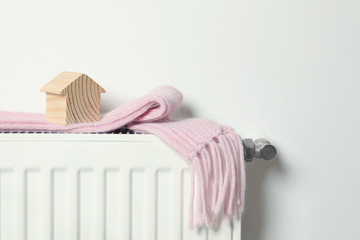 House model and pink scarf on radiator indoors, space for text. Winter heating efficiency