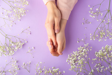 Obraz na płótnie Canvas Flat lay. Tender female hands with white delicate flowers. On a purple background. Art photo, top view, horizontal photo.