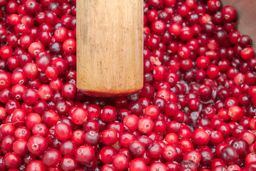 Crush the red cranberry berries with a wooden rolling pin