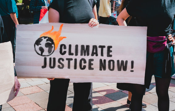 The phrase " Climate justice now " drawn on a carton banner in woman's hand. Protest for ecology. Human holds a cardboard with an inscription: Climate justice now