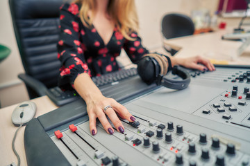Female sound engineer in a radio broadcast studio. It controls the sound in the mixing console.