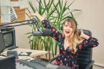 Beautiful young woman leads a live show on a radio station, sitting in front of the sound of a...