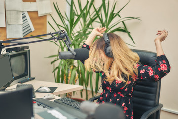 Beautiful young woman leads a live show on a radio station, sitting in front of the sound of a...