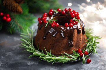 Christmas chocolate bundt cake with glaze decorated with fresh berries and rosemary. Winter baking at Xmas or New Year with decorations on dark background