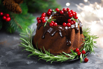 Fototapeta na wymiar Christmas chocolate bundt cake with glaze decorated with fresh berries and rosemary. Winter baking at Xmas or New Year with decorations on dark background