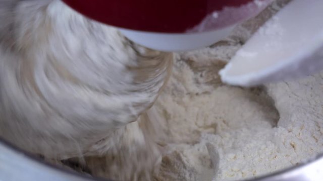 Preparation of homemade bread - The kitchen mixer mixes the dough and occasionally a small amount of flour is added