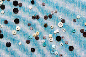 Sewing composition with many randomly arranged white and dark buttons on blue fabric cloth.