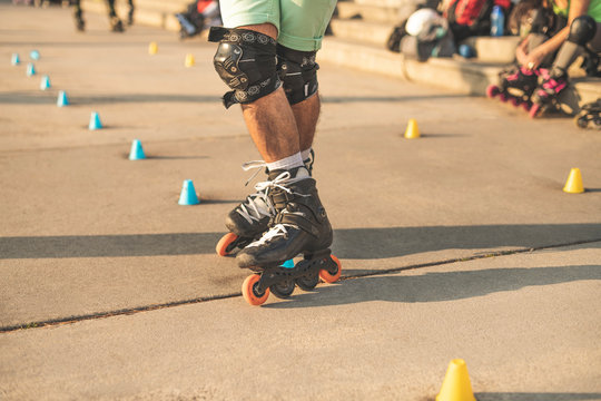 Close-up view of the rollers of a caucasian man, doing rollerblading, inline skating, performing on a slalom course on asphalt surface. Small cones for training on the road.