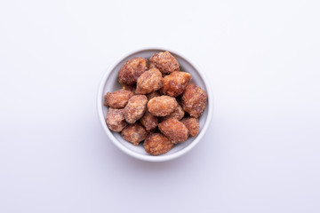 Peanuts praline sweet in a white bowl, on white background, soft light, copy space