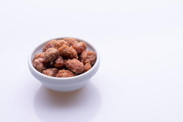Peanuts praline sweet in a white bowl, on white background, soft light, copy space