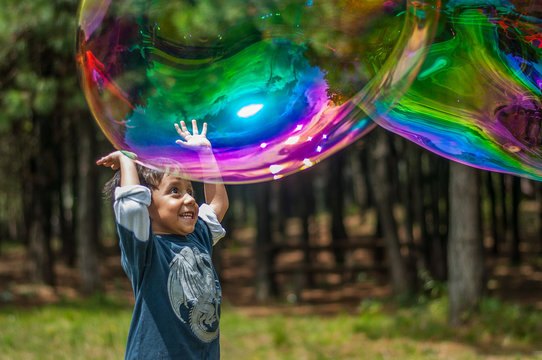 niño latino jugando burbujas de jabon en el campo, sonriente, felicidad