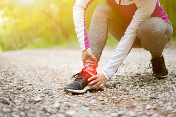 sport runner woman cramps in leg and feel pain, athletic young Asian girl in sportswear touching her muscles ankle painful injury outside after exercise workout in nature road. Sports injuries concept