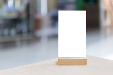 Mock up Label the blank menu frame in Bar restaurant ,Stand for booklets with white sheets paper acrylic tent card on wooden table cafeteria blurred background can inserting the text of the customer.