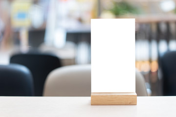 Mock up Label the blank menu frame in Bar restaurant ,Stand for booklets with white sheets paper acrylic tent card on wooden table cafeteria blurred background can inserting the text of the customer.