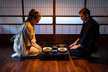 Young couple seiza sitting on hardwood floor pillows at traditional Japanese in ryokan kaiseki...