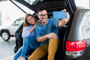 Beautiful excited young couple at car showroom taking selfie photo in their new car.