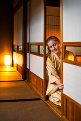Traditional Japanese home or ryokan room with gaijin caucasian woman in kimono, tabi socks opening shoji sliding paper doors sitting on tatami mat floor