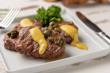 Filet mignon with caper and mustard sauce, broccoli, pepper grinder on wooden white background,...