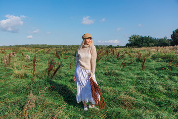 Happy beautiful blond woman walking in a green field with a bouquete of dry brown plants