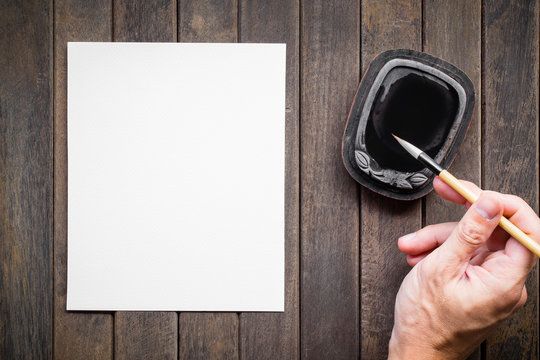 Abstract man hand white paper with bamboo calligraphy brush and inkstone on old wooden table. picture for add text or greeting card chinese new year. Chinese traditional painting 