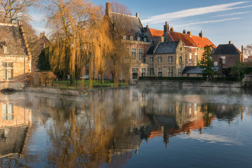 Fototapeta na wymiar Heritage brick building with autumn tree reflect into lake in Minnewater park, Bruges, Belgium