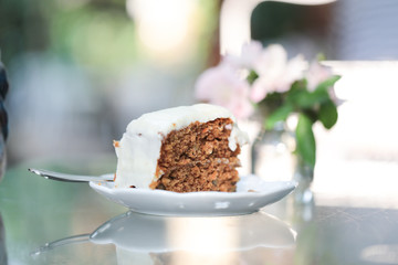 A piece of carrot cake with creamy white chocolate on white ceramic plate with steel spoon