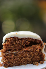 A piece of carrot cake with creamy white chocolate on white ceramic plate with steel spoon
