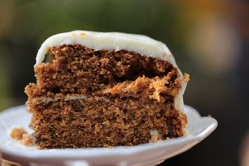 A piece of carrot cake with creamy white chocolate on white ceramic plate with steel spoon