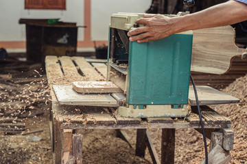 Carpenter planing a piece of  wood using the wood planning machine at workshop in carpentry and woodworking project