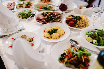 Wedding table, food, drinks, water. Table with silver and glass stemware at restaurant before starting to celebrate a wedding. Cheese, meat, salads. The holiday table
