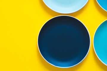 Colorful pastel blue ceramic plates isolated on yellow background. Top view.