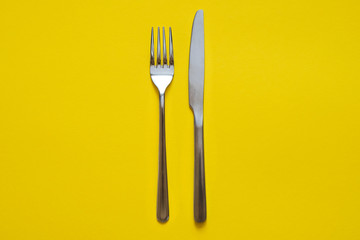 Fork and knife isolated on yellow background. Top view.