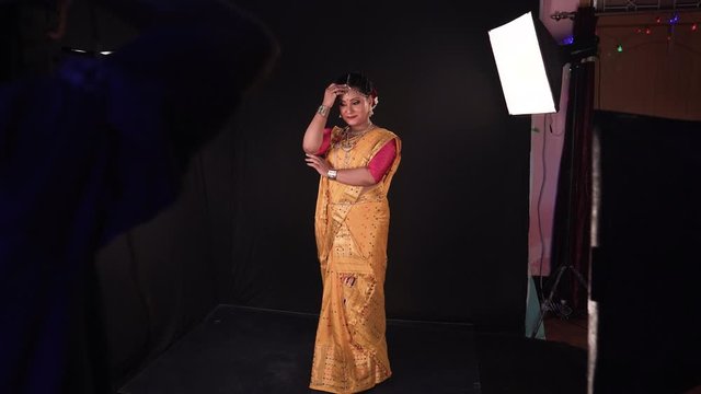 Female model dressed in tradiotional Indian dress in red and gold standing still at photo session