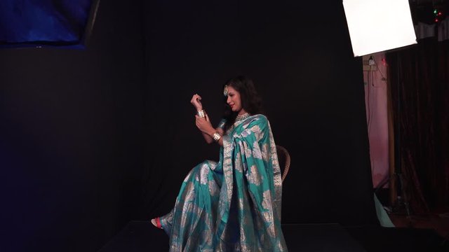 Indian Female model posing in traditional dress with hands up while sitting on a chair