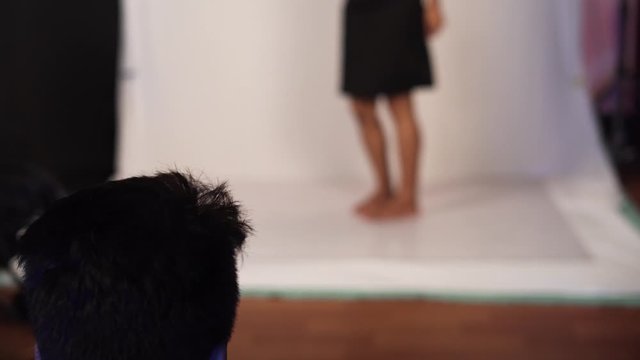 Close look of male photographer taking pictures and filming young beautiful woman in black dress against white background