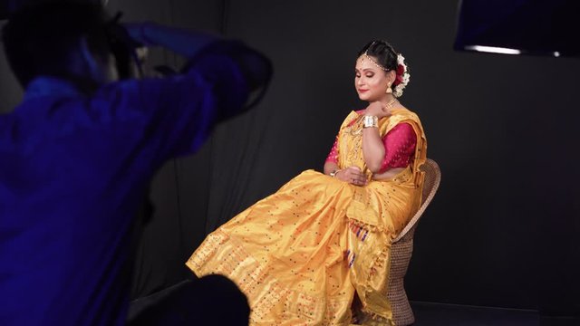 Gorgeous Indian model sitting on a chair with tradition dress in gold and red colors