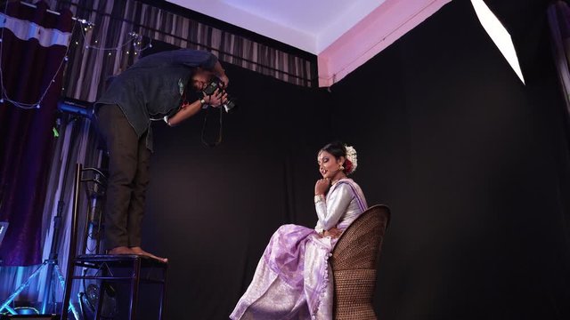Low angle view of photographer taking ohotos of gorgeous Indian model sitting on a chair in studio