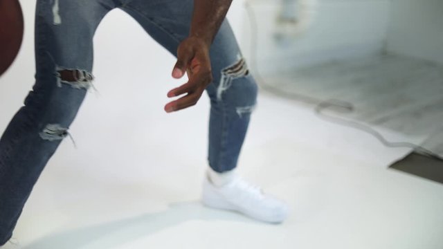 Slow Motion shot of an African American dribbling a basketball. Shot in a studio with a white background. The man is wearing a non-brand inspiring shirt with the message "Be You" on it.