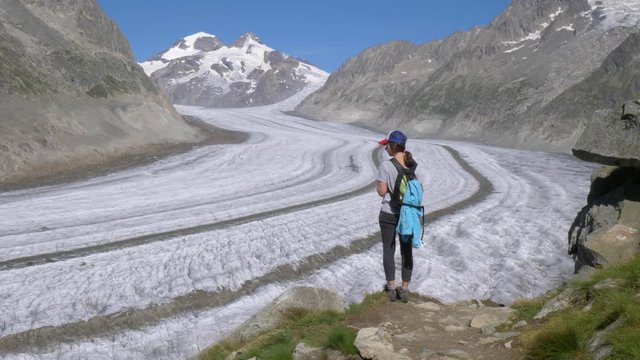 A lone female hiker looks toward a vast glacier. She stops on the trail edge to stop and look in awe at the vast mountains and glacier that surround her.