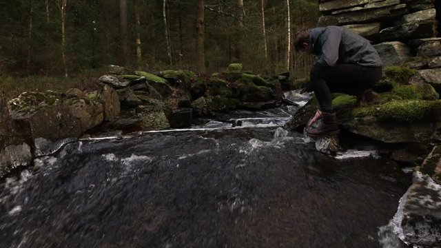 Young man sitting by a small creek running through the woods near Halland, Sweden, during winter time