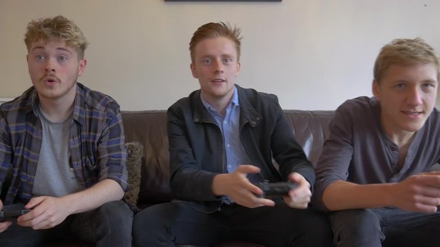 Friends hanging out playing video games with wireless controllers. Boys having fun playing video competitive games.