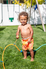 Smiling Cute little boy splashing playing in the sprinklers in the backyard. African American boy playing in the outdoors on a warm summer day