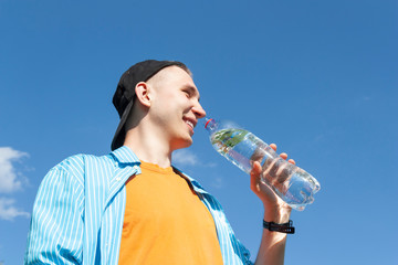 Guy drinking water from a bottle against a blue sky