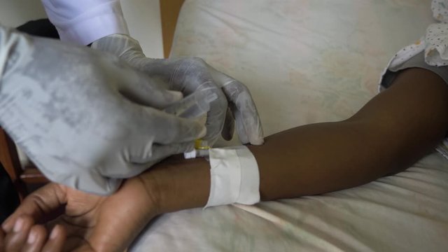 Close up of an African woman's hand with a cannula in it and a doctor injecting medicine into her arm.