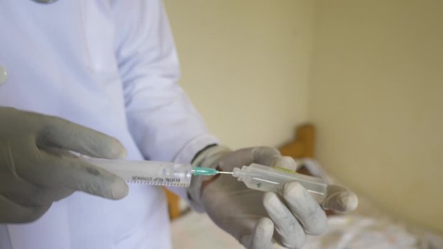 A close up shot of a African doctor wearing gloves preparing medicine into a needle in Africa.