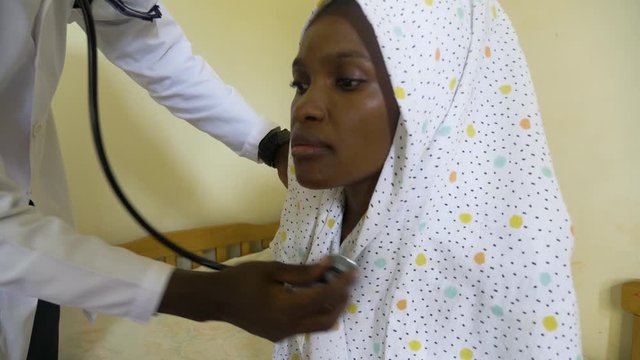 Close up shot of a African woman getting her chest checked with a stethoscope in a small medical clinic.
