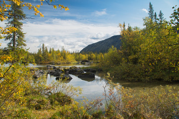 Misty morning on a small mountain lake with a scattering of boulders, reflecting dense clouds, surrounded by autumn forest. Background.