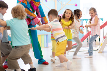 Obraz premium Clown bawi dzieci w wieku przedszkolnym na przyjęciu urodzinowym. Drużyny dziecięce rywalizują ze sobą radośnie ciągnąc linę